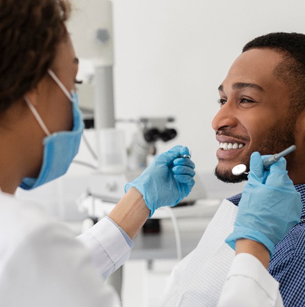 Dentist using tools to examine smiling patient's teeth