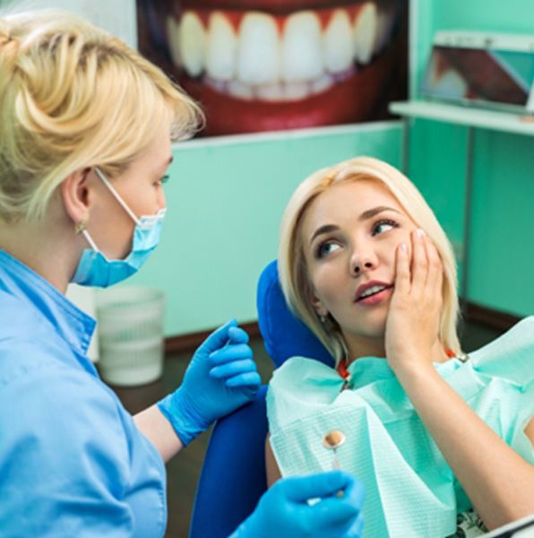 A woman holding her cheek while talking to her dentist