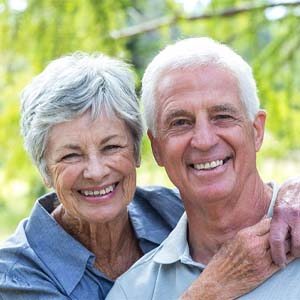 Older couple smiling with woman’s arms around man outside