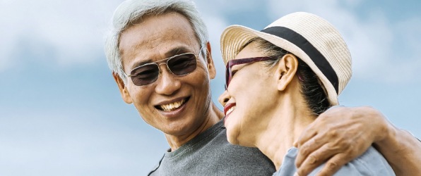Older couple smiling together after replacing missing teeth